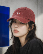 Chica con gorra Core burdeos junto a un panel azul