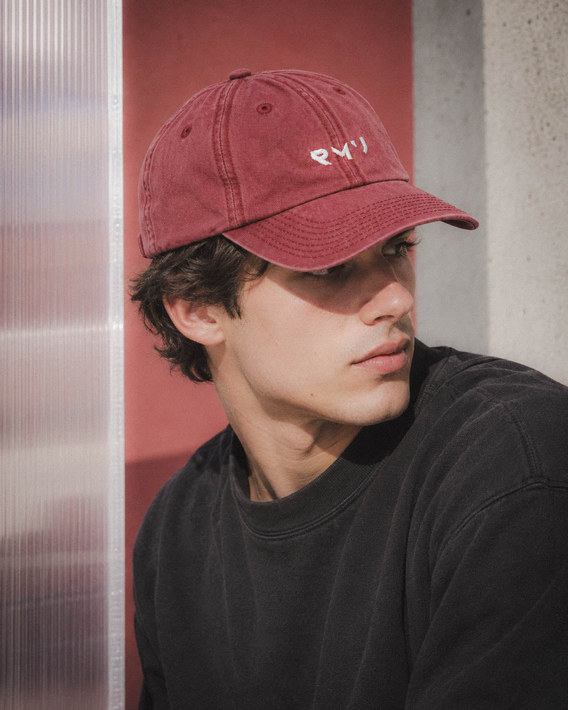 Chico con gorra Core burdeos junto a un panel rojo