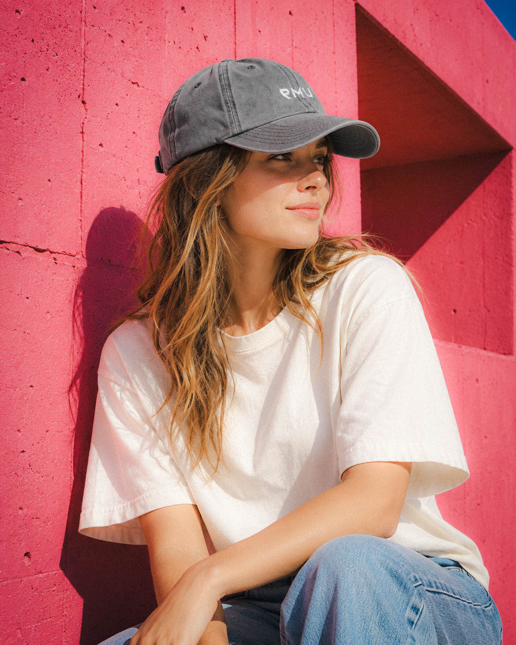 Chica con gorra Core gris oscuro y camiseta blanca junto a un panel rojo
