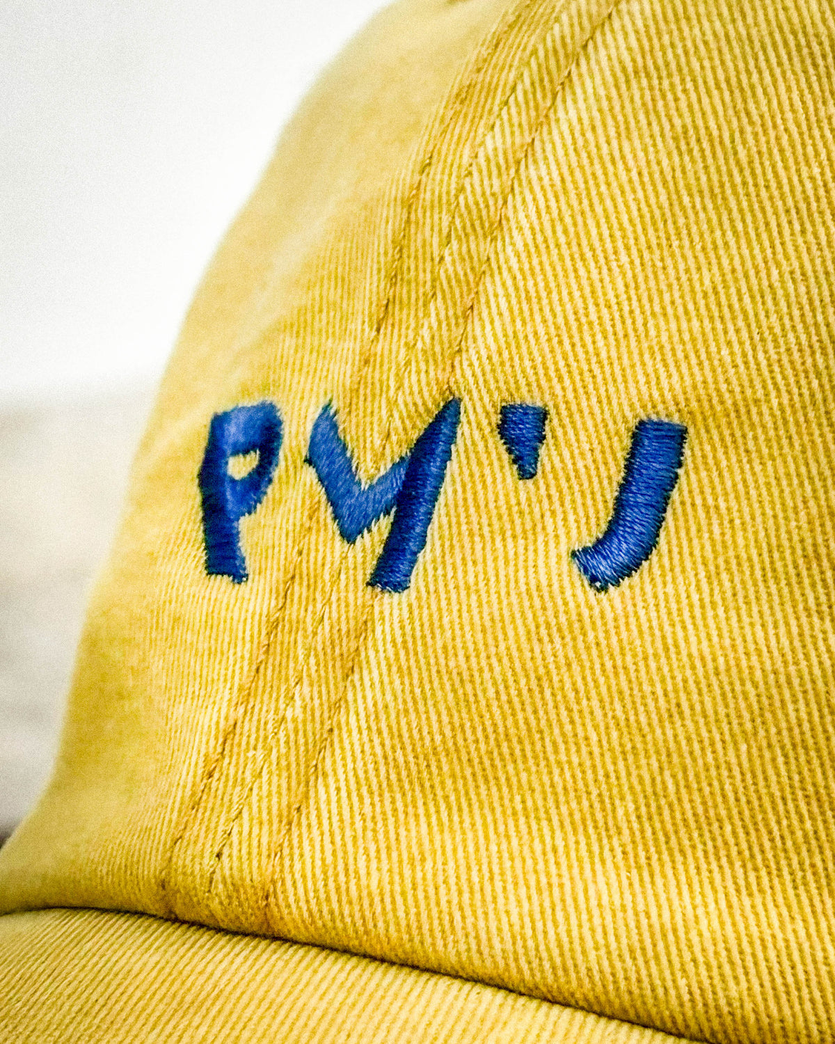 Detalle del logotipo RMU bordado en azul sobre la gorra Core mostaza