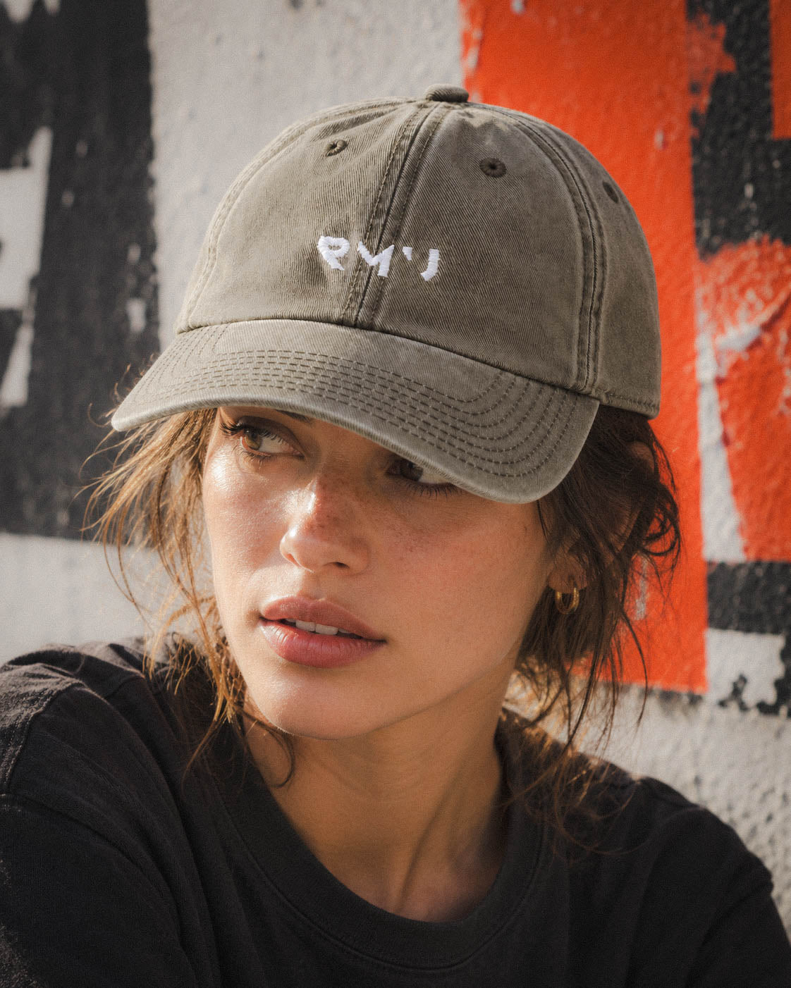 Chica con gorra Core verde oliva junto a un panel naranja