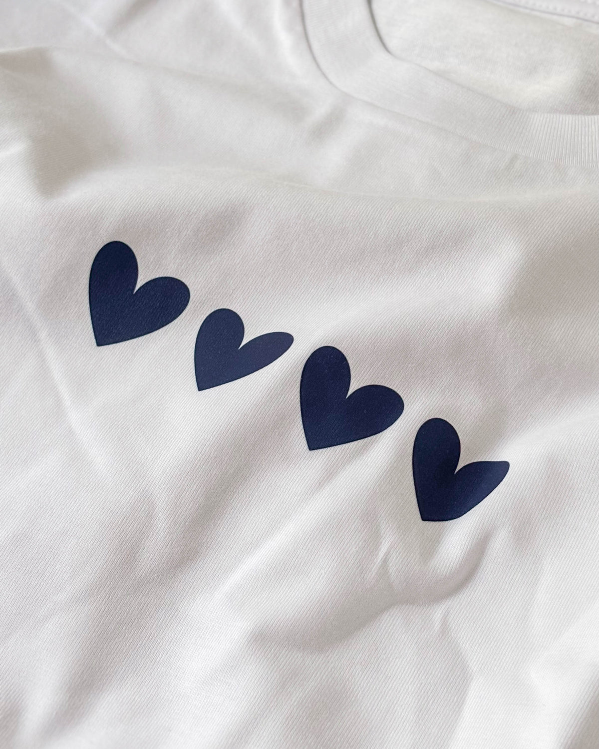 Fotografía real del tejido blanco y los cuatro corazones azul marino de la camiseta Four Hearts