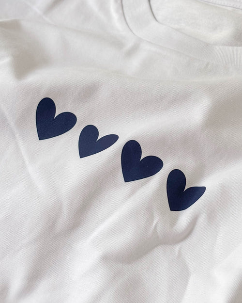 Fotografía real del tejido blanco y los cuatro corazones azul marino de la camiseta Four Hearts