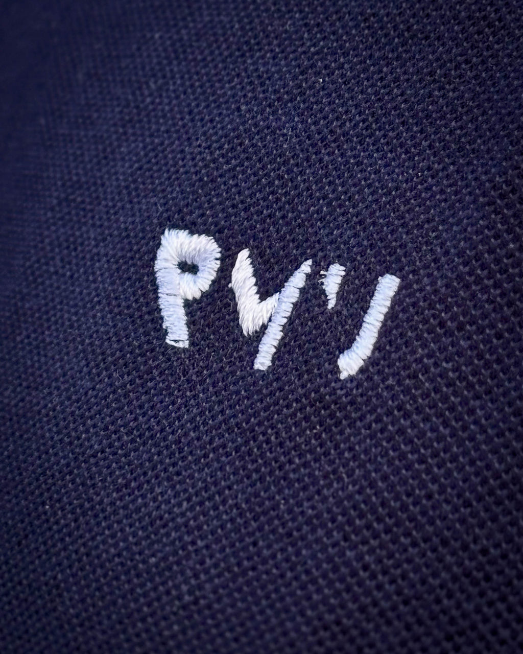 Detalle del bordado blanco RMU y del tejido piqué del polo Core azul marino