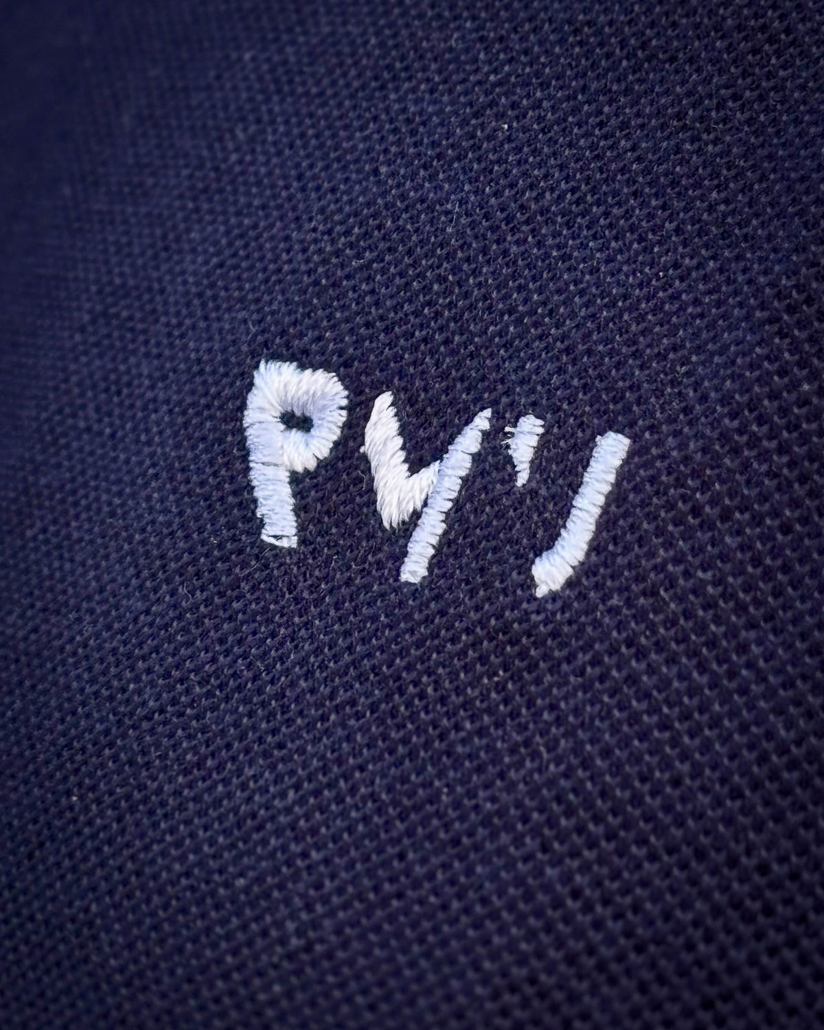 Detalle del bordado blanco RMU y del tejido piqué del polo Core azul marino