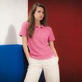 Laura con polo Core fresa y bordado RMU blanco junto a paneles azules y burdeos