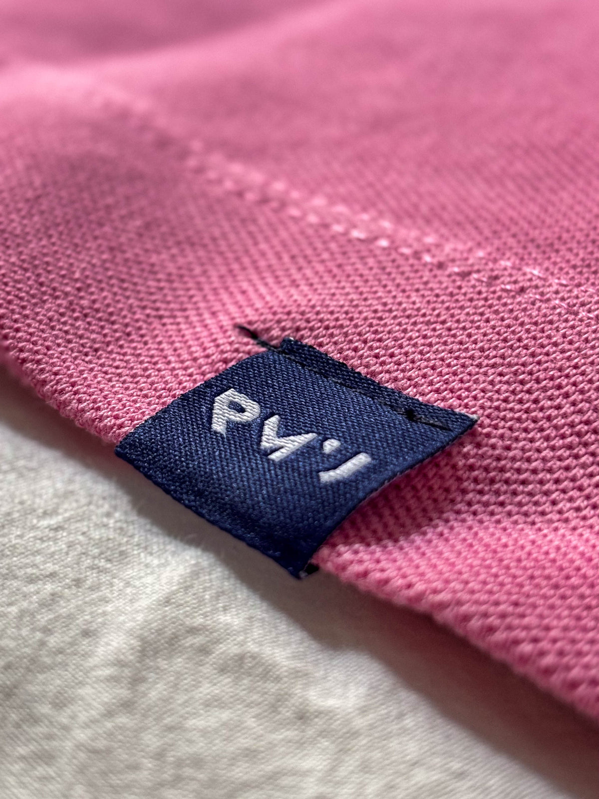 Detalle de la etiqueta azul navy RMU cosida en el bajo del polo Core Fresa