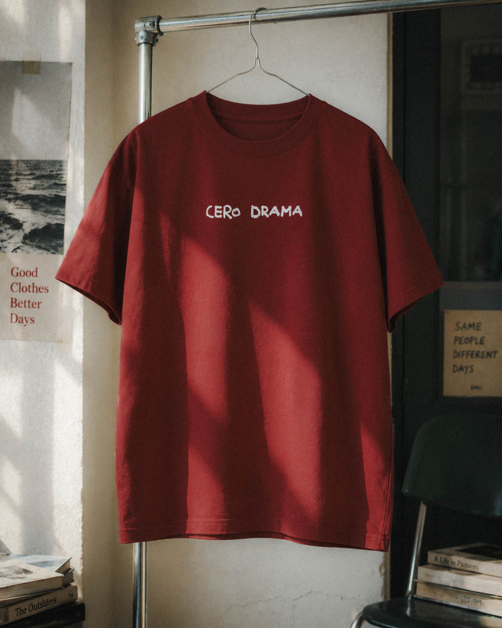 Camiseta Cero Drama burdeos colgada en una composición interior con libros