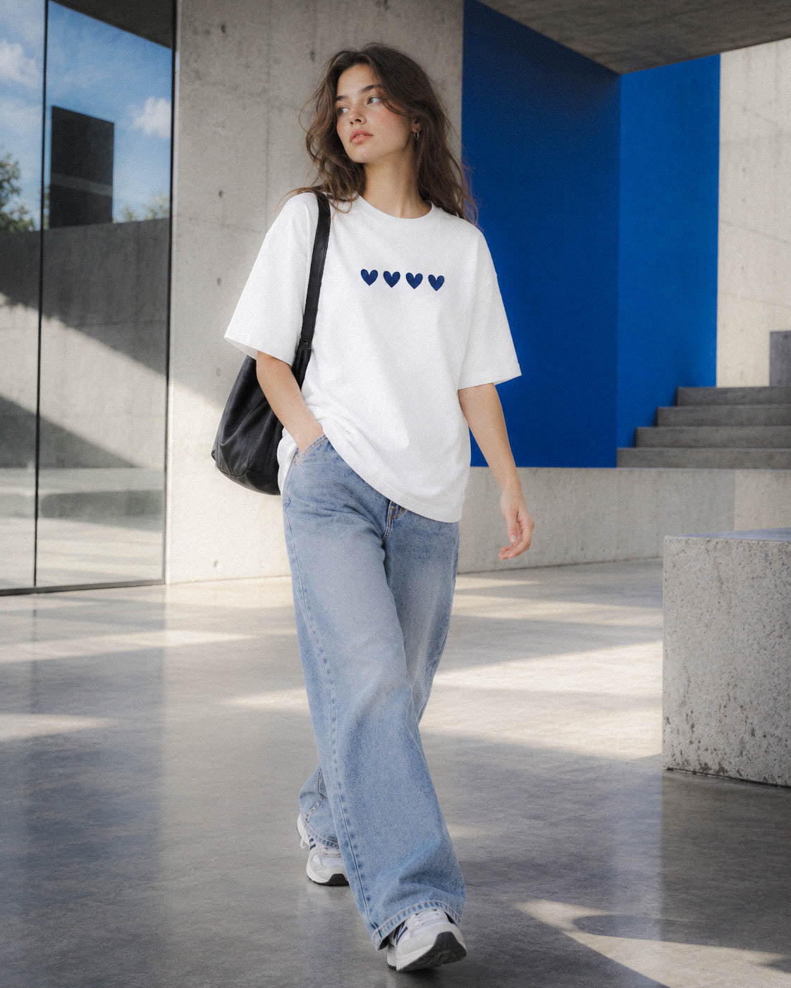 Chica con camiseta Four Hearts y bolso negro caminando junto a unas escaleras