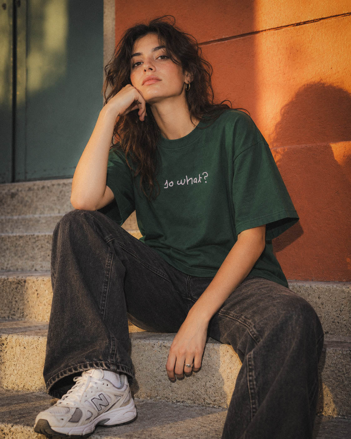 Chica con camiseta So What verde sentada junto a un panel naranja
