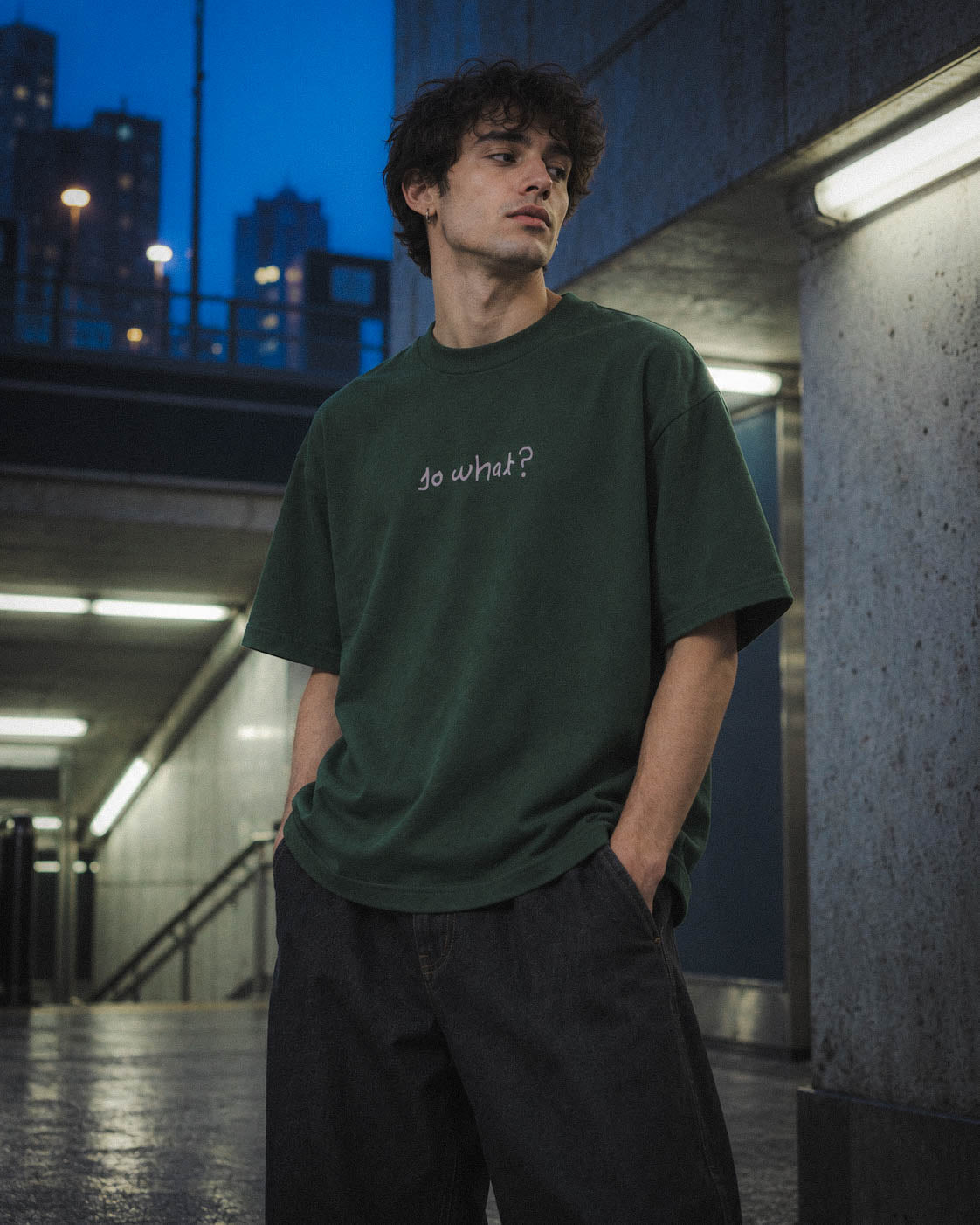 Chico con camiseta So What verde en unas escaleras al anochecer